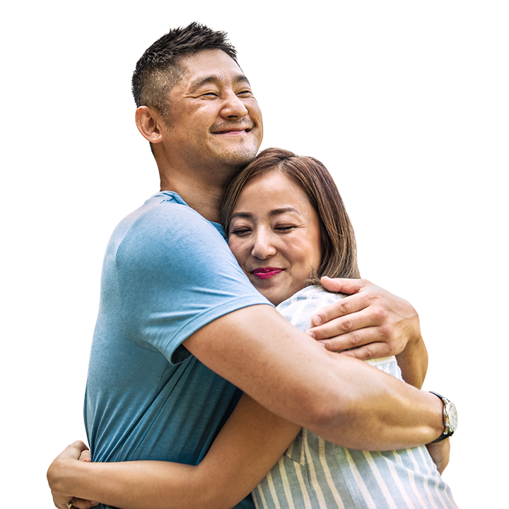 middle aged Asian couple hugging happily in their driveway with their new house behind them